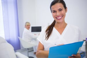Portrait of smiling dentist writing a medical report in clinic Portrait of smiling dentist writing a medical report in clinic